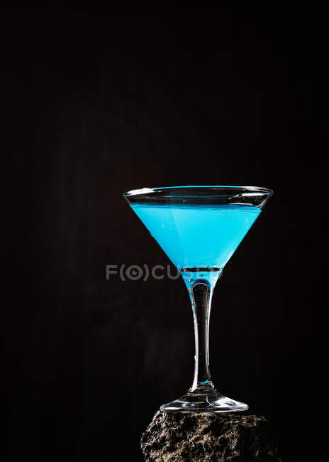 Синій коктейль лагуни в кристалі елегантного скла розміщений на грубій поверхні на чорному тлі. — стокове фото