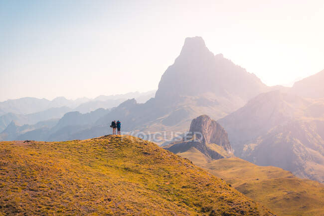 Distant anonymous hikers standing on grassy hilltop while admiring rough mountain range against cloudless sky in nature of Spain — Stock Photo
