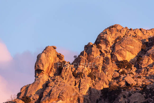 Pierres brutes recouvertes de mousse et d'arbustes situées au sommet d'une montagne enneigée dans le parc national de la Sierra de Guadarrama à Madrid, Espagne au coucher du soleil — Photo de stock