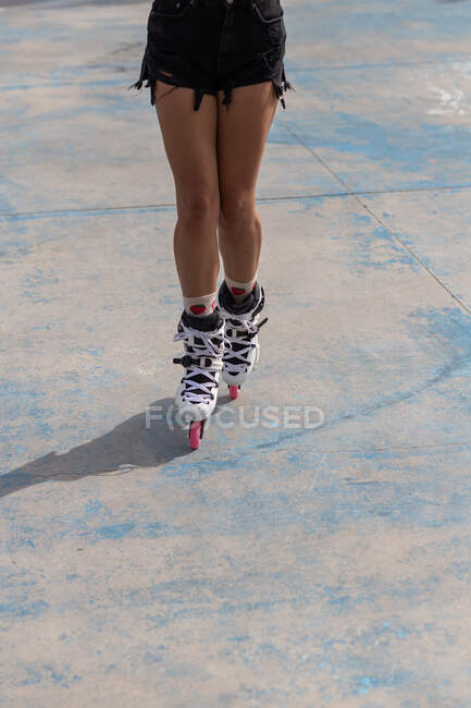Cultivo anónimo piernas femeninas en patines blancos con ruedas rosas de pie sobre pavimento de hormigón en skate park - foto de stock