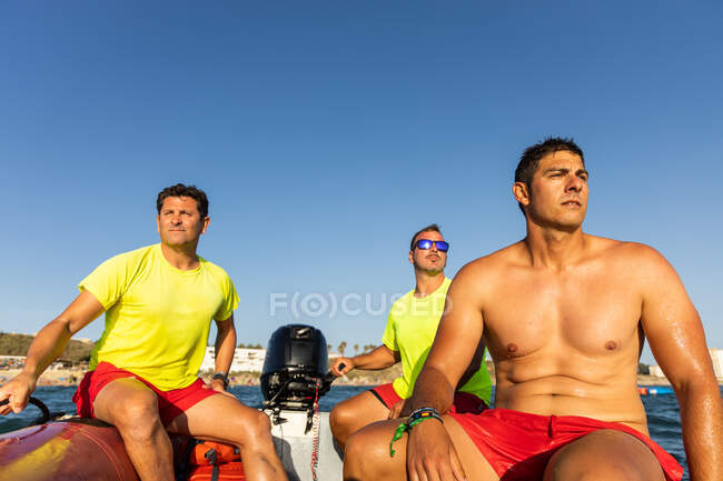 Lifeguards sitting on inflatable motorboat floating on rippling blue sea and controlling safety on sea — Stock Photo