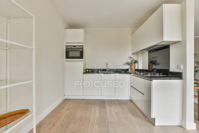 В светлой современной кухне новой квартиры расположены простые белые шкафы с гардеробами — стоковое фото