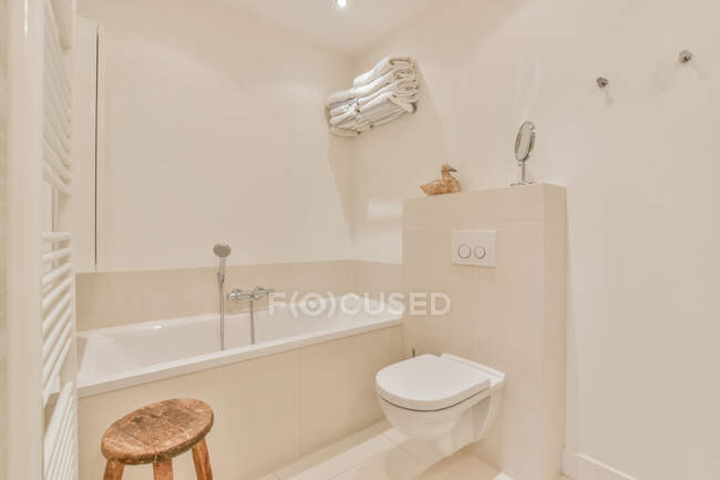 Design criativo do banheiro com vaso sanitário e banquinho contra banheira com chuveiro em casa de luz — Fotografia de Stock