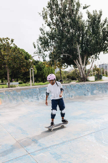 Повне тіло молодої етнічної людини в повсякденному вбранні в захисному шоломі з колінними подушечками і ліктями катання на скейтборді в скейтборді парку — стокове фото