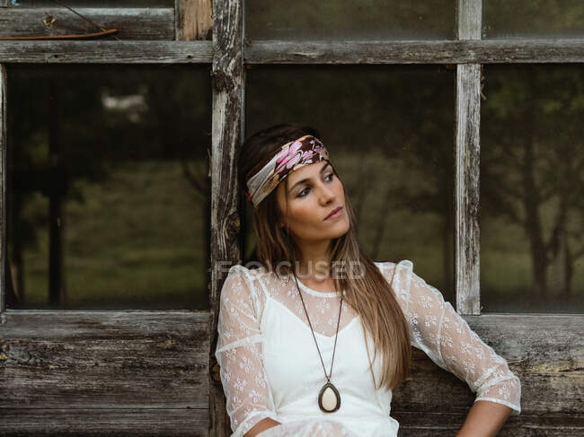 Mujer hippie sentada en el porche de su cabaña mirando hacia otro lado - foto de stock