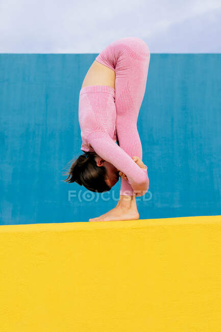 Side view of unrecognizable fit female in pink sportswear standing on yellow mat while stretching body during workout — Stock Photo