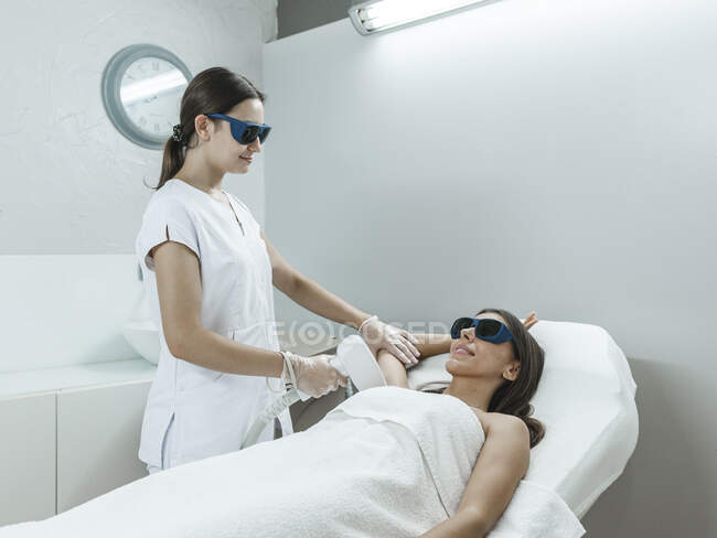 Young master in goggles doing laser hair removal procedure with professional equipment in hand in light salon — Stock Photo
