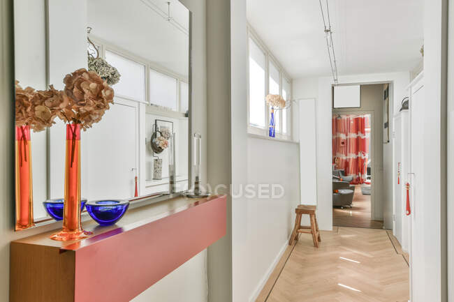 Couloir avec fenêtres et vases décorés colorés menant à la chambre avec fauteuils dans un appartement lumineux avec des murs blancs et chaise en bois — Photo de stock