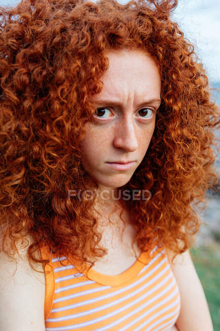 Femme bouleversée avec des cheveux bouclés au gingembre montrant une émotion de mécontentement et regardant la caméra — Photo de stock