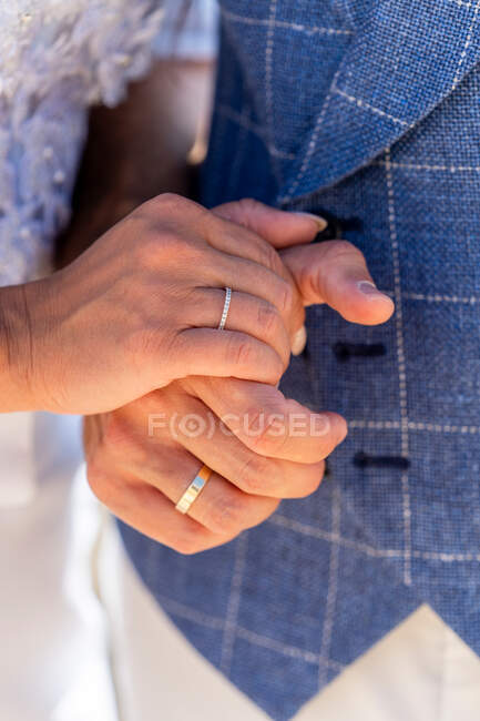 Crop pareja casada sin rostro en trajes de novia tomados de la mano con anillos de boda a la luz del día - foto de stock