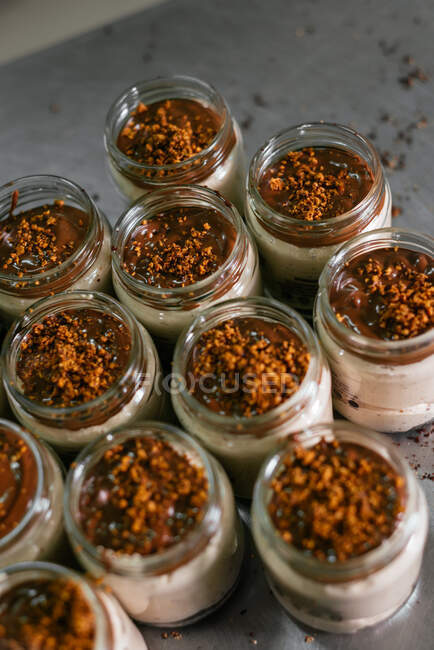 From above glass jars with delicious layer dessert with white cream decorated with caramel topping and crushed nuts served on table in kitchen — Stock Photo