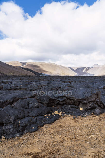 Pintoresco paisaje de lava negra seca en terreno accidentado del volcán activo Fagradalsfjall bajo el cielo nublado en Islandia durante el día - foto de stock
