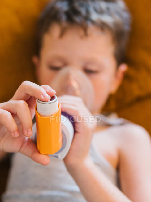 De conteúdo acima menino doente usando respirador e respiração de oxigênio do inalador enquanto deitado no sofá em casa — Fotografia de Stock