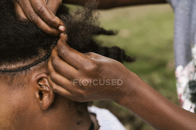Cultivar mulher africana irreconhecível tecendo trança tradicional para amigo feminino anônimo no campo — Fotografia de Stock