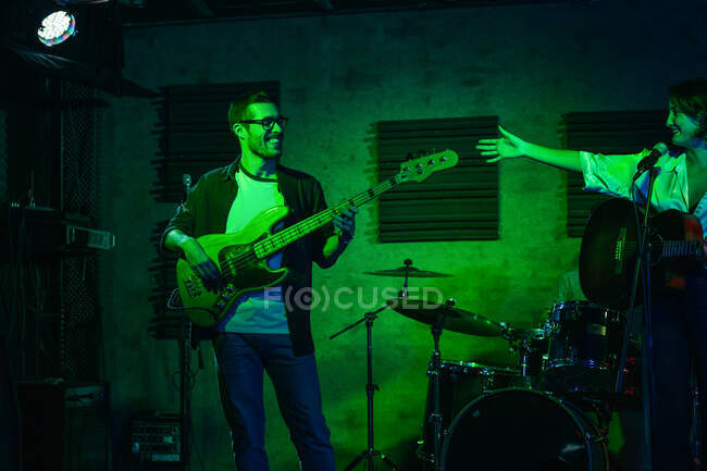 Hombre tocando la guitarra mientras mujer cantando y cantando canción en el club con luces de neón - foto de stock