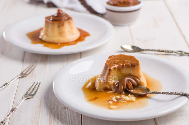 Fresh egg custard topped with sweet dulce de leche served with syrup on wooden table with cutlery in kitchen — Stock Photo