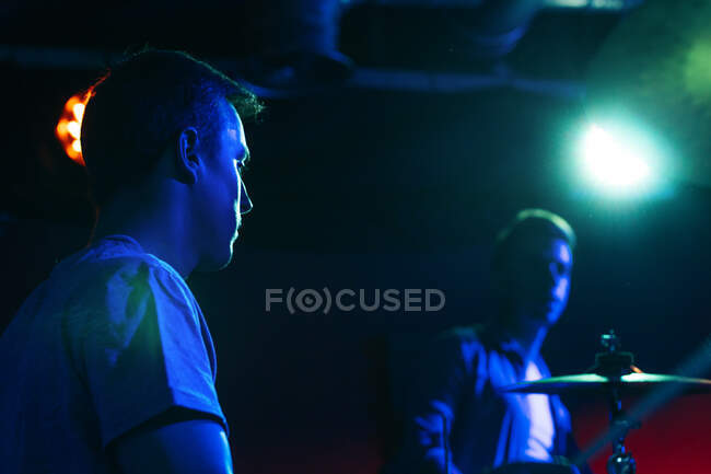 Sérieux jeunes gars jouant de la musique à la batterie dans un club avec des néons — Photo de stock