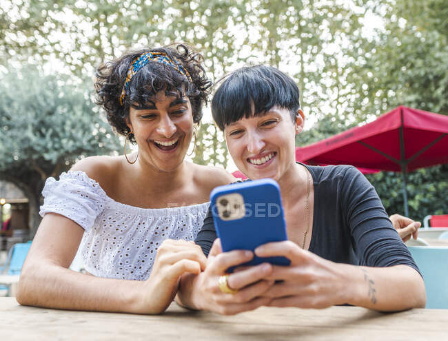 Content friendly multiracial females browsing on mobile phone while enjoying weekend together in summer park — Stock Photo