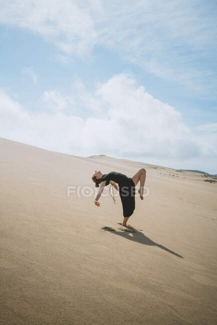 Ganzkörper-Seitenansicht einer barfüßigen Tänzerin, die die Arme ausstreckt, während sie sich nach hinten beugt und das Bein in der sandigen Wüste hebt — Stockfoto