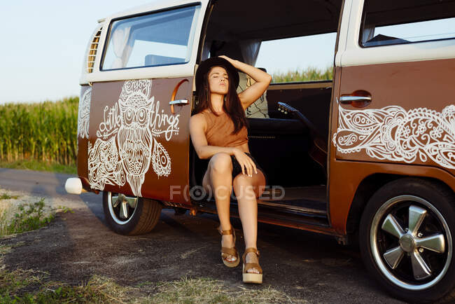 Приваблива брюнетка дівчина з капелюхом сидить на підлозі вінтажного фургона в сонячний день — стокове фото