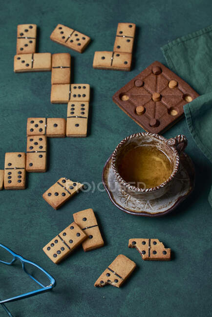 Draufsicht auf leckere süße Domino-Kekse auf grünem Hintergrund mit Tasse Heißgetränk und Schokoladengebäck — Stockfoto