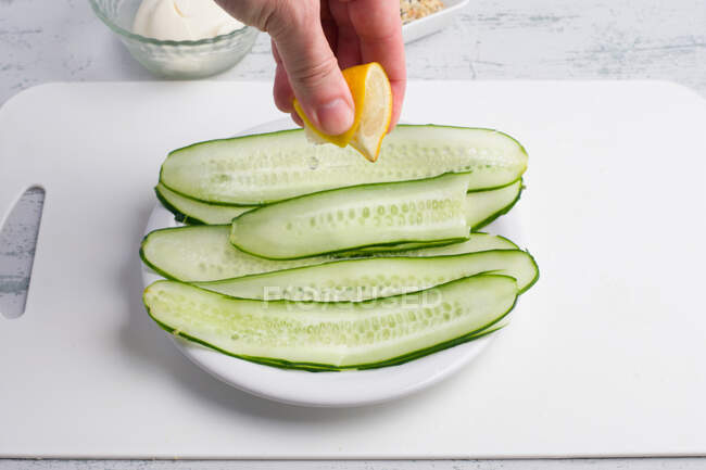 Crop unrecognizable chef squeezing fresh lemon juice on fresh cucumber slices served on plate on table — Stock Photo