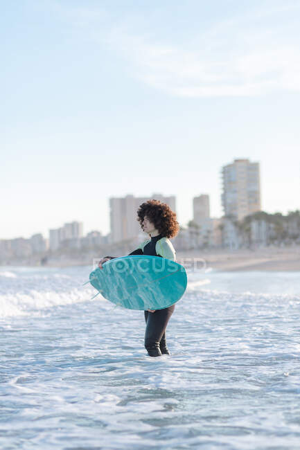 Seitenansicht einer jungen Surferin im Neoprenanzug auf winkendem Meerwasser mit Brett, die den Sommertag genießt — Stockfoto
