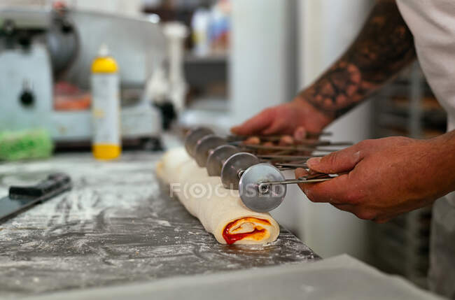 Вид сбоку на неузнаваемый шеф-повар, стоящий у кухонного стола и разрезающий сырой пирог сладким сиропом — стоковое фото