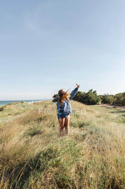 Чорно-біла анонімна жінка в сорочці, що стоїть з піднятими руками на трав'янистому лузі під безхмарним небом влітку — стокове фото