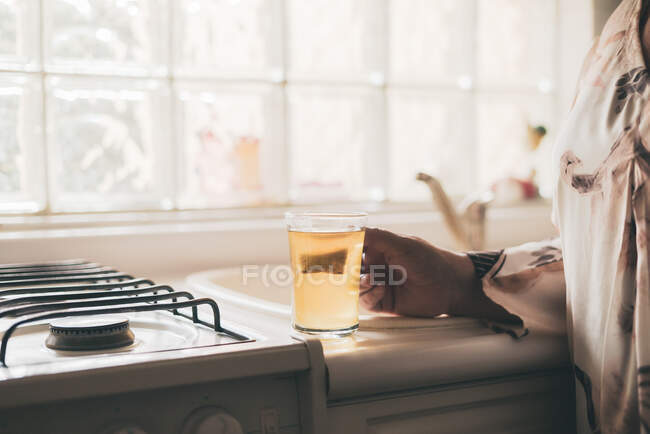 Cropped unrecognizable adult female wearing silk blouse and trousers brewing tea bag in glass mug kitchen — Stock Photo