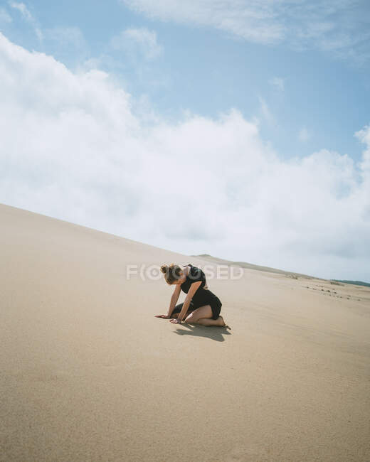 Side view full body of barefoot female leaning on hands while kneeling on sandy dune in hot desert — Stock Photo