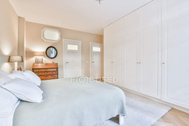 Bed with cover and pillows against doors and white closet in house with lamps and mirror — Stock Photo