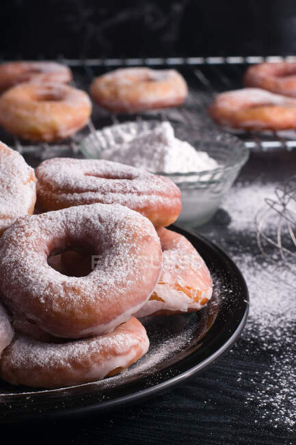 Sweet fried doughnuts served on plate near metal cooling rack a on black messy table with powdered sugar — Stock Photo
