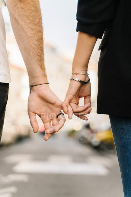 Visão traseira da colheita casal romântico irreconhecível segurando pequenos dedos enquanto caminhava na rua no dia ensolarado na cidade — Fotografia de Stock