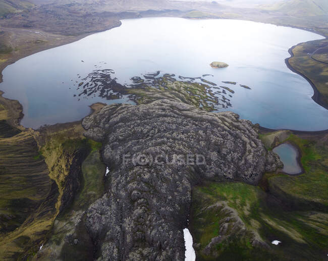 Desde arriba de la costa cubierta de hierba con formaciones rocosas ásperas cerca de lago tranquilo situado en Islandia en el día de verano en la naturaleza - foto de stock