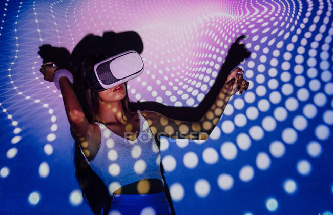 Femme à la mode dans le crop top expérience de la réalité virtuelle dans le casque tout en dansant dans les projecteurs lumières — Photo de stock