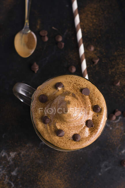 De arriba vaso de café dulce Dalgona con cobertura espumosa servido en la mesa con rollo de oblea de chocolate y cacao en polvo - foto de stock