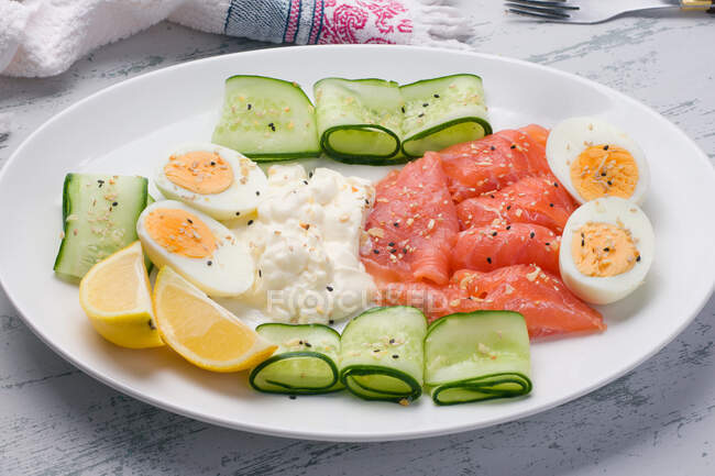 Von oben Räucherlachs und Frischkäse auf Teller serviert mit gekochten Eiern und Gurkenscheiben für leckeres Mittagessen — Stockfoto