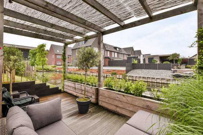 Veranda mit Sofa und Sessel auf Holzboden mit Topfbaum gegen Wohnhäuser tagsüber — Stockfoto