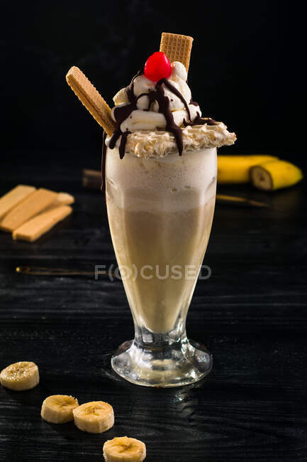 Ein Glas süßer Bananen-Milchshake garniert mit Schlagsahne-Waffeln und Kirsche mit Schokolade obendrauf — Stockfoto