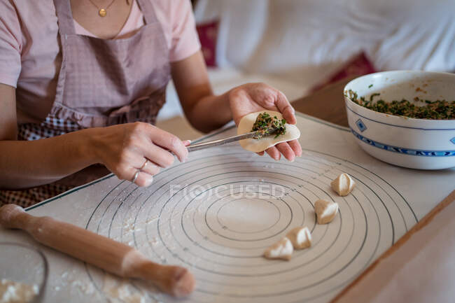 De cima de colheita mulher irreconhecível em roupas casuais e avental recheando bolinhos com carne enquanto prepara jiaozi chinês tradicional na cozinha — Fotografia de Stock