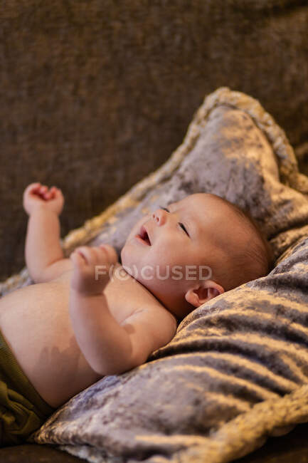 High angle of adorable upset shirtless baby crying while lying on soft cushion on comfortable sofa at home — Stock Photo