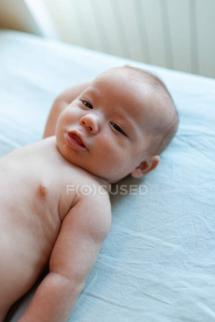 Nettes glückliches Baby mit kurzen Haaren im gestreiften Body lächelnd, während es am sonnigen Morgen auf einem bequemen Bett liegt — Stockfoto