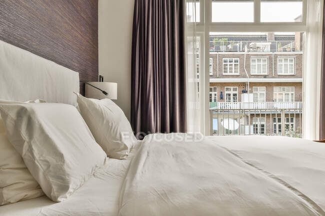 Комфортабельная кровать и минималистский стиль располагаются у окна с шторами в современной спальне — стоковое фото