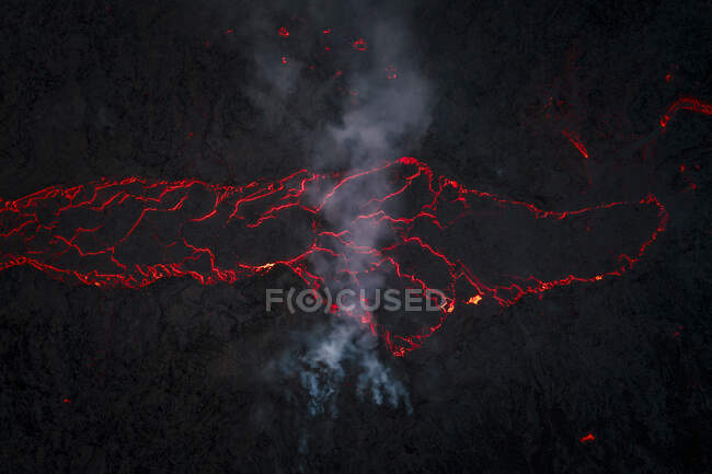 Vista superior del magma rojo caliente que fluye en la superficie montañosa oscura por la noche en las tierras altas de Islandia en la oscuridad - foto de stock
