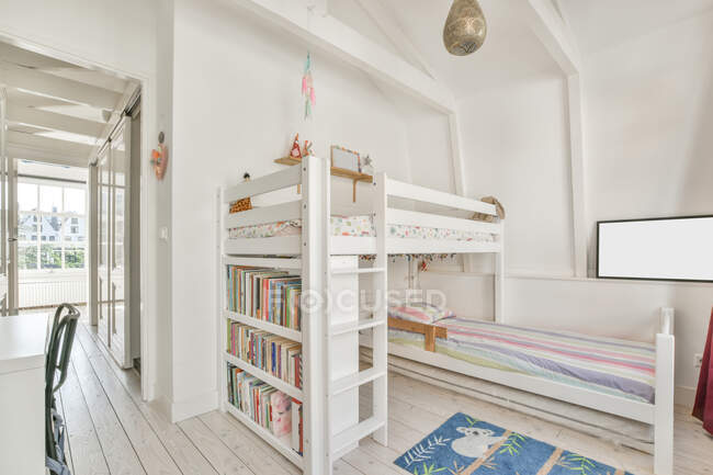White bunk bed with bookshelves and colorful carpet near doorway in light modern children bedroom — Stock Photo