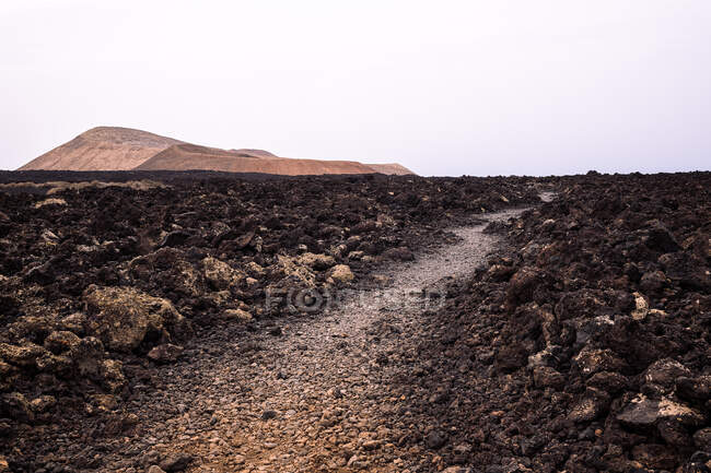 Rota áspera entre lava escura contra os vulcões Caldera Blanca e Caldereta no Parque Natural das Ilhas Canárias de Lanzarote Espanha — Fotografia de Stock
