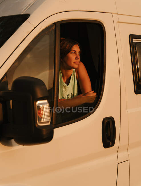Femme voyageuse sereine regardant par la fenêtre de la caravane et profitant du coucher du soleil pendant le voyage en Espagne — Photo de stock