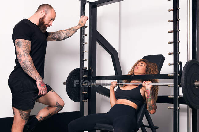 Concentrated strong sportswoman lifting heavy barbell with weights during functional workout with instructor in gym — Stock Photo