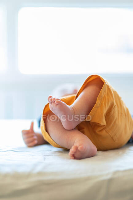 Анонимный милый босоногий ребенок лежит один на удобной кровати в солнечное утро дома — стоковое фото